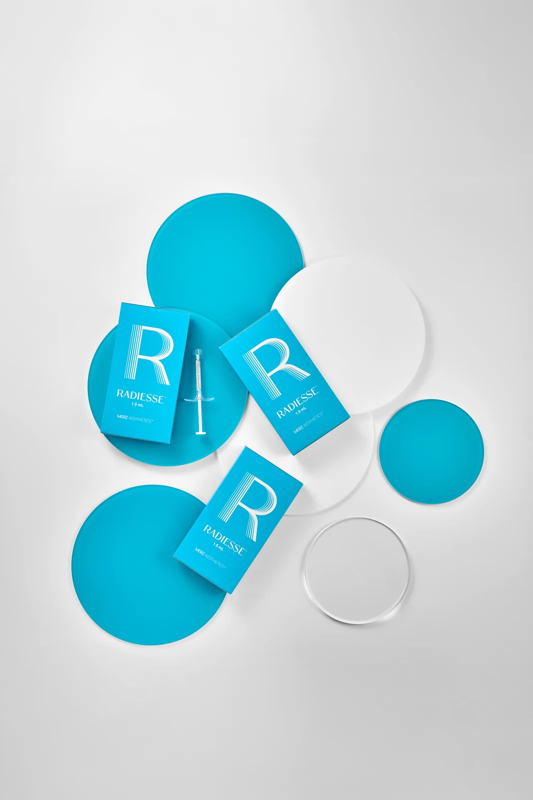 Three Radiesse cartons and a syringe arranged on blue and clear discs, seen from above