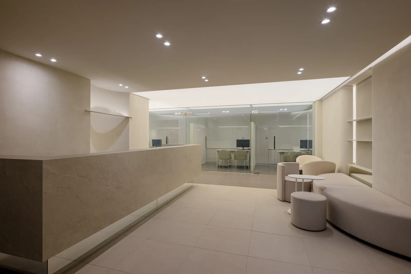 Lobby of Dear Clinic Cheongdam — stone reception counter, bouclé lounge seating and glass-walled consultation rooms