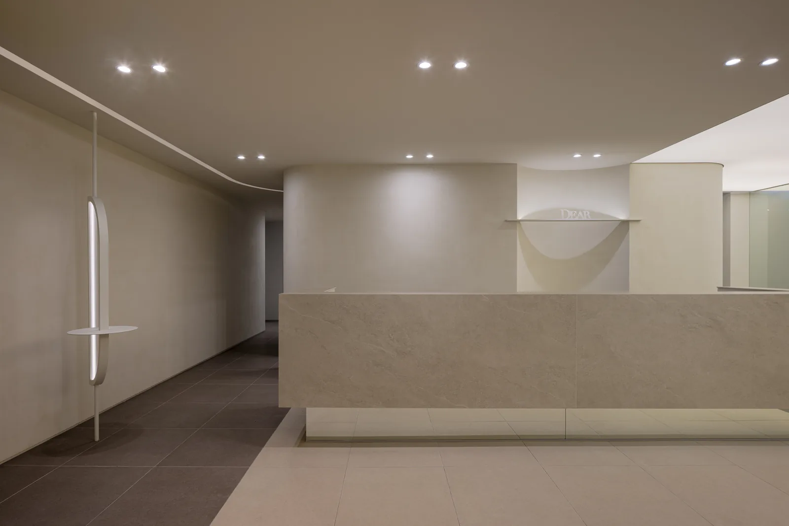 Reception desk at Dear Clinic in Cheongdam, Gangnam, Seoul, with the backlit DEAR sign on a curved plaster wall