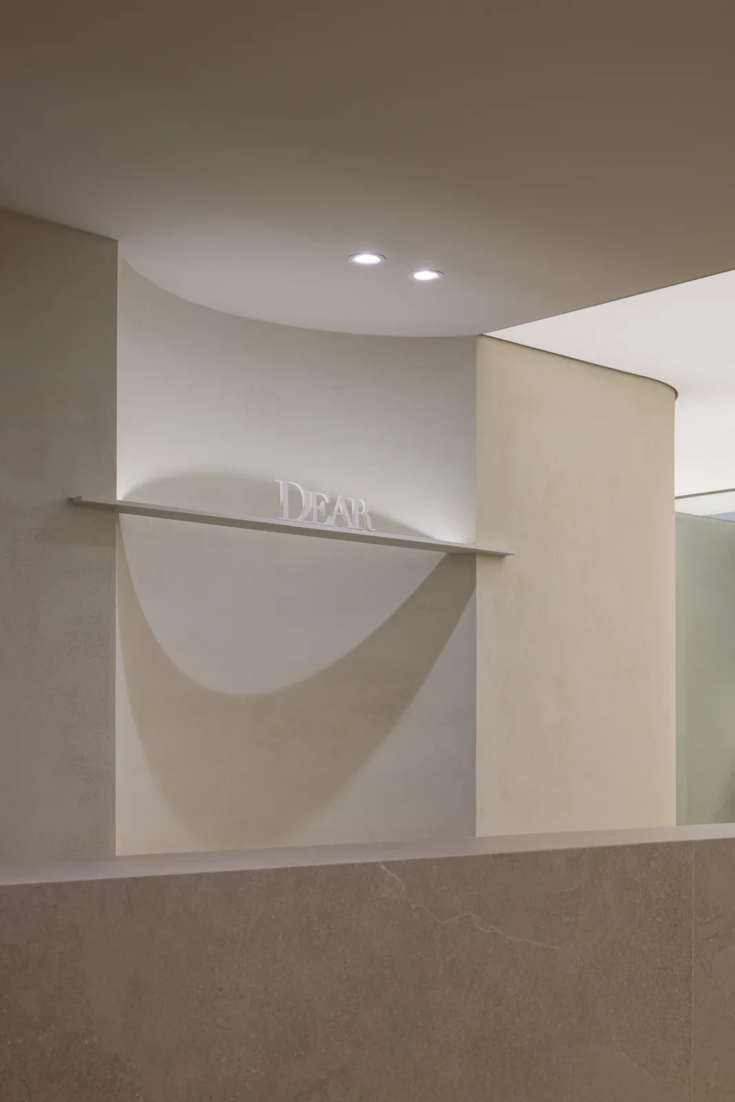 The DEAR wordmark lit on a curved plaster wall inside Dear Clinic