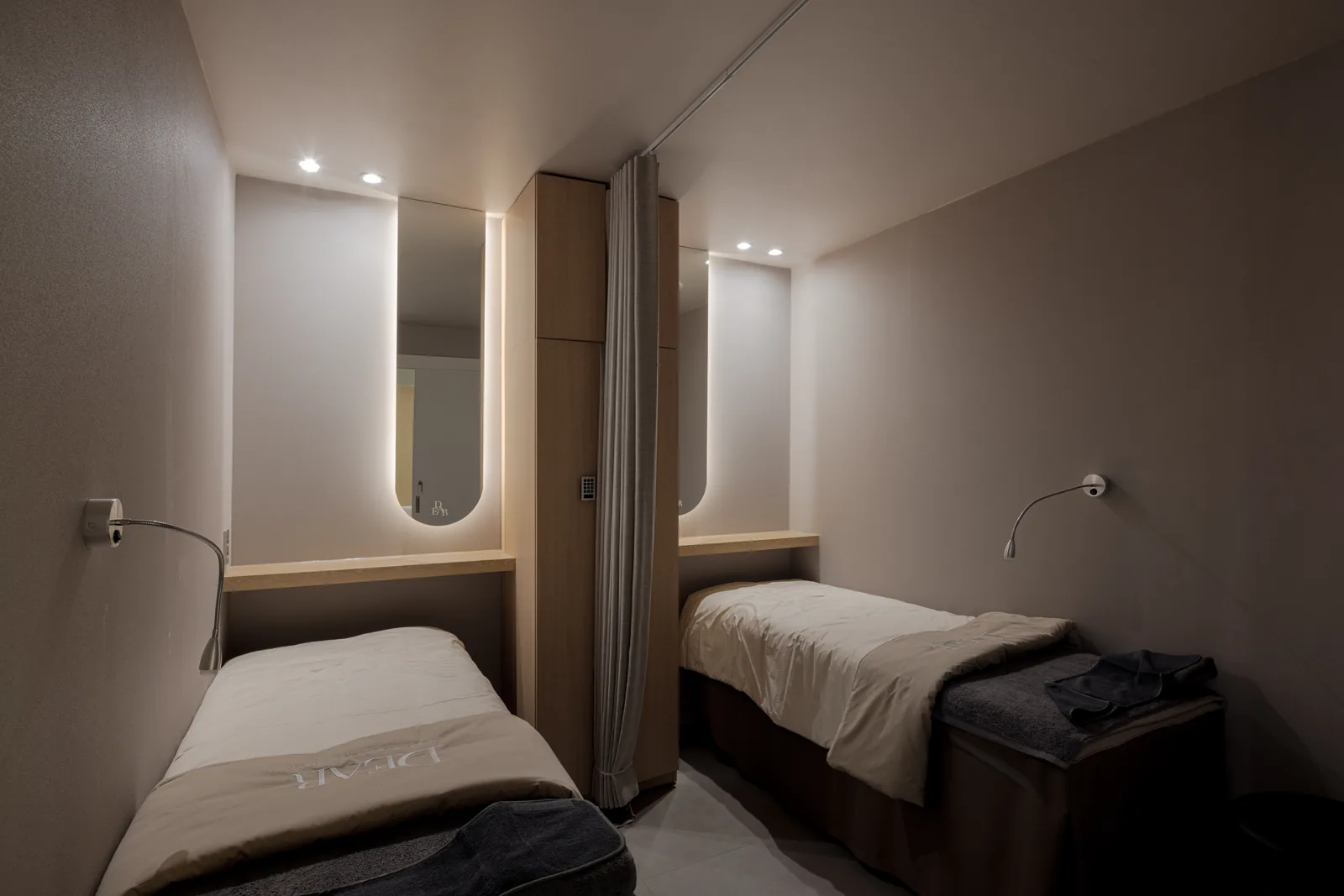 Twin recovery room at Dear Clinic with two beds, backlit arch mirrors and oak cabinetry