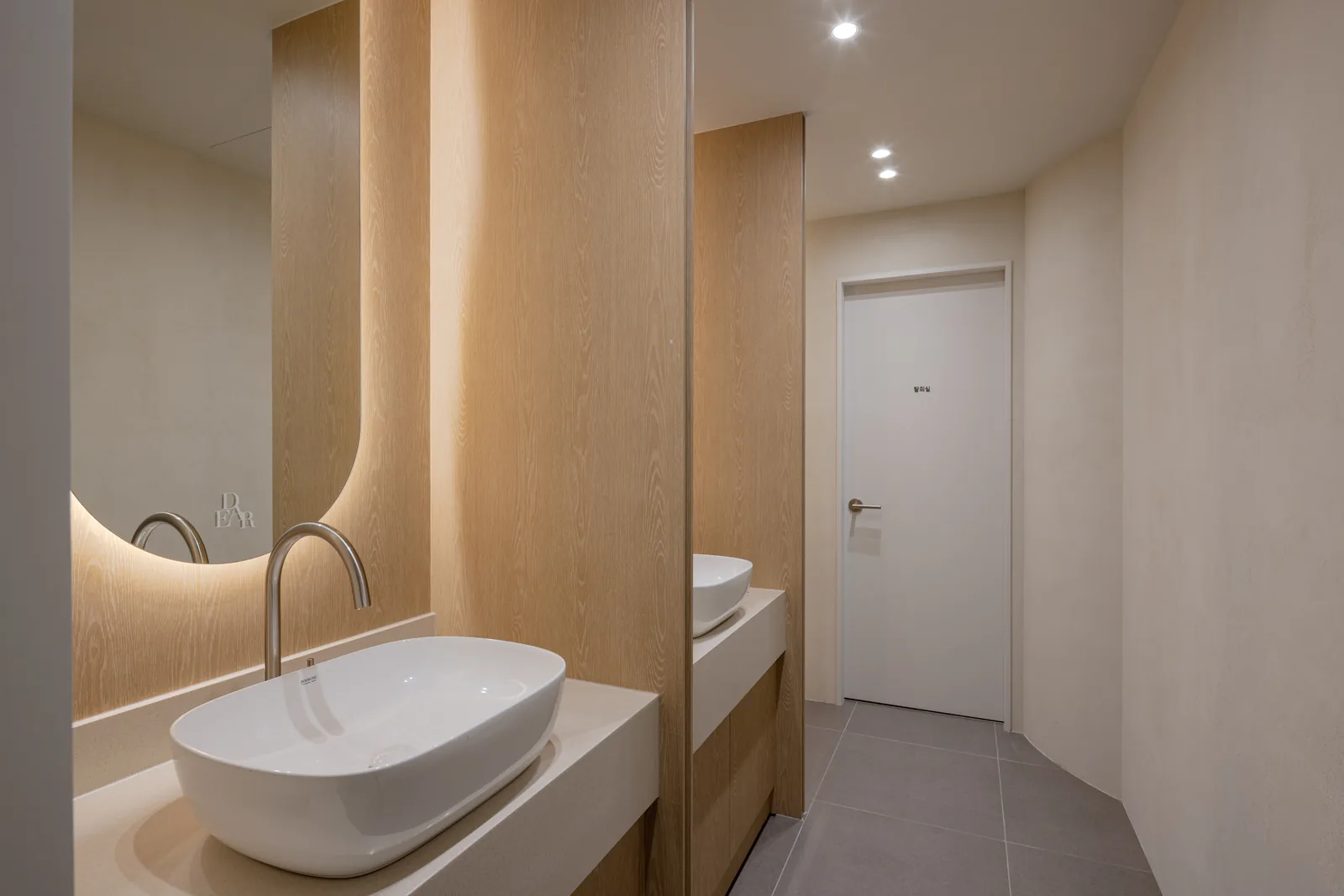 Powder room at Dear Clinic with twin basins and a backlit mirror carrying the DEAR mark
