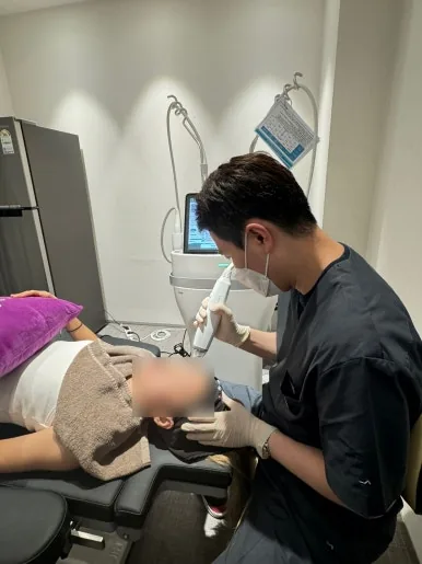 Practitioner applying a treatment handpiece to a patient's cheek at Dear Clinic